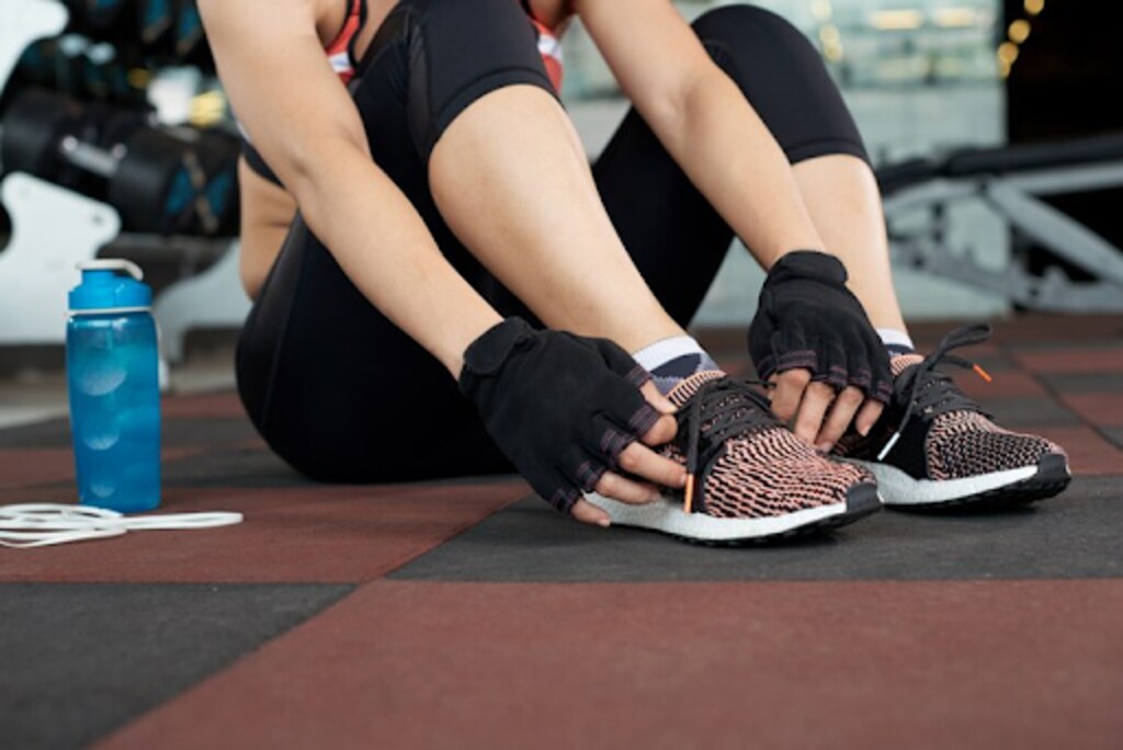 woman in activewear sitting on the gym floor tying shoes laces