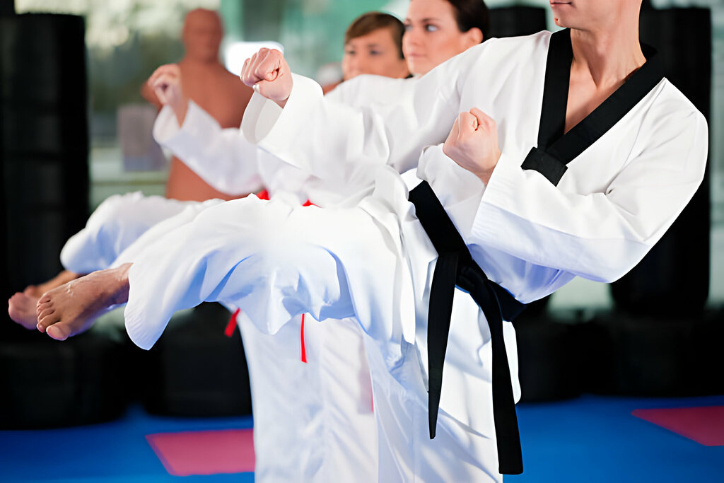 People in a gym in martial arts training exercising Taekwondo, the trainer has a black belt
