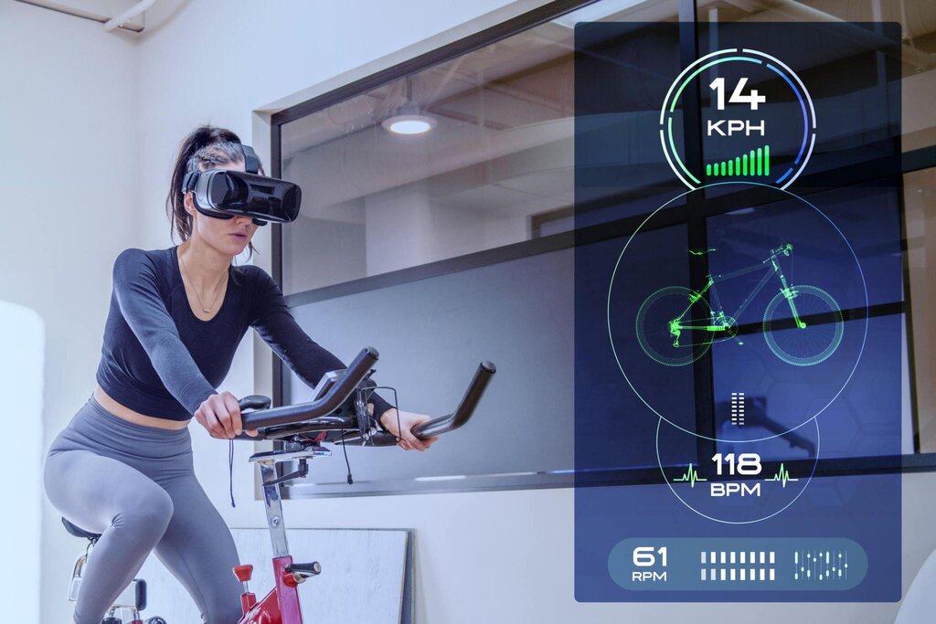Woman sitting on a stationary bike wearing a virtual reality headset to watch the progress of her ride and calculate distance, calories burned, and speed.