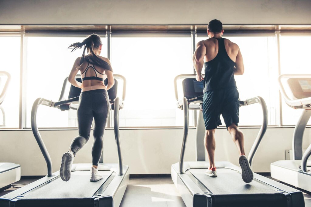 Back view of beautiful sports people running on a treadmill in gym.